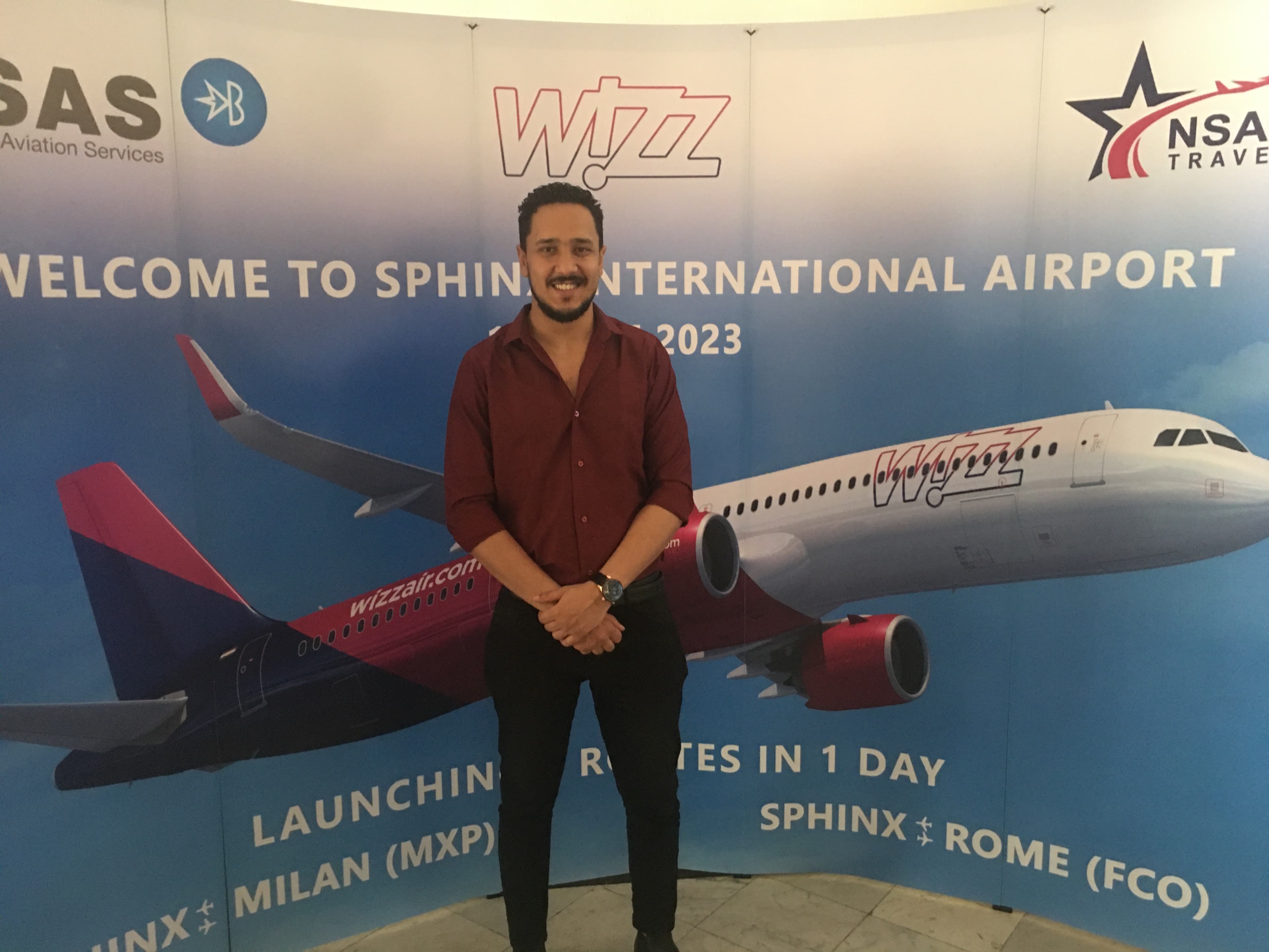 Mostafa Ahmed at Sphinx International Airport — Wizz Air inaugural flight activation with branded backdrop featuring route launch details for Milan and Rome